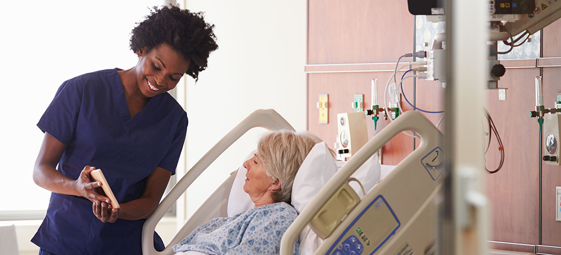 Nurse talks to patient in bed.