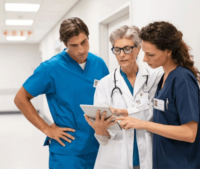 Two nurses and a doctor look at a document in a hallway.