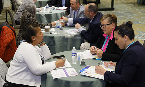 A group at a table talks to each other while writing on paper.