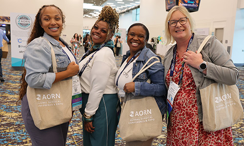 A group of 4 women stand together with AORN tote bags.